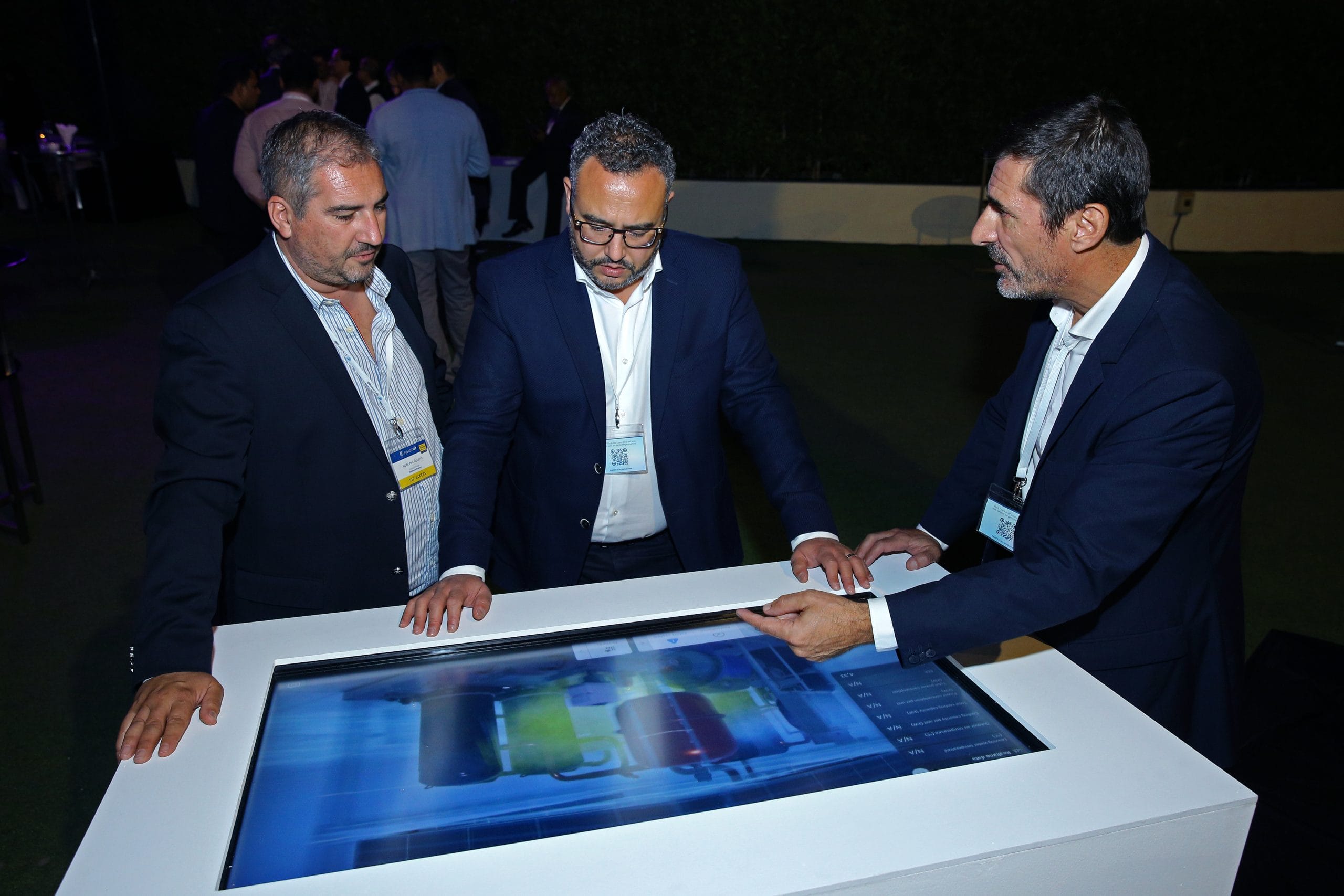 Three men discussing HVAC systems being displayed on a touchscreen at an exhibition