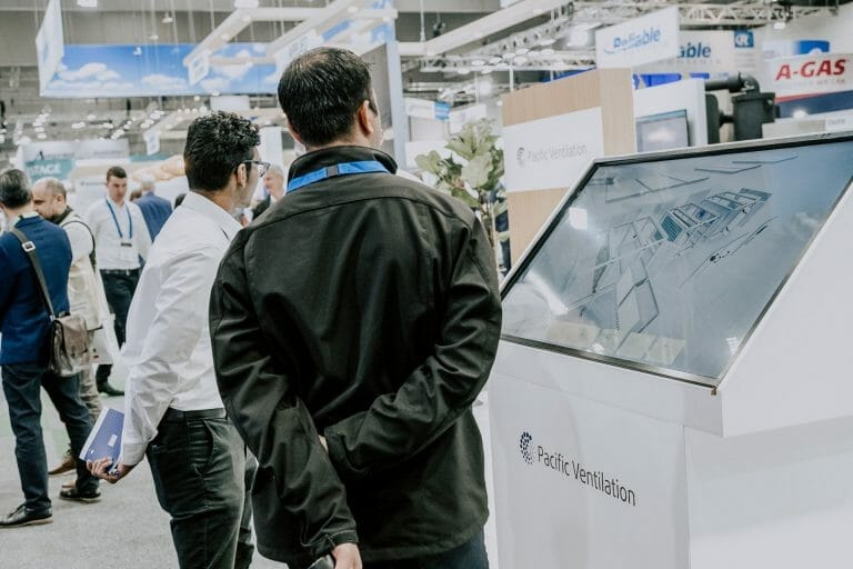 Two men at a pacific ventilation exhibition stand observing their 3D VR interactive application on a touchscreen